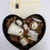 Box de regalo con forma de corazón abierto con taza blanca, café, miel, cookies y frutos secos junto a su tapa con moño.