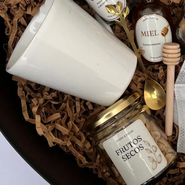 Primer plano de taza de cerámica, frasco de frutos secos y cuchara dorada de diseño en box corazón.