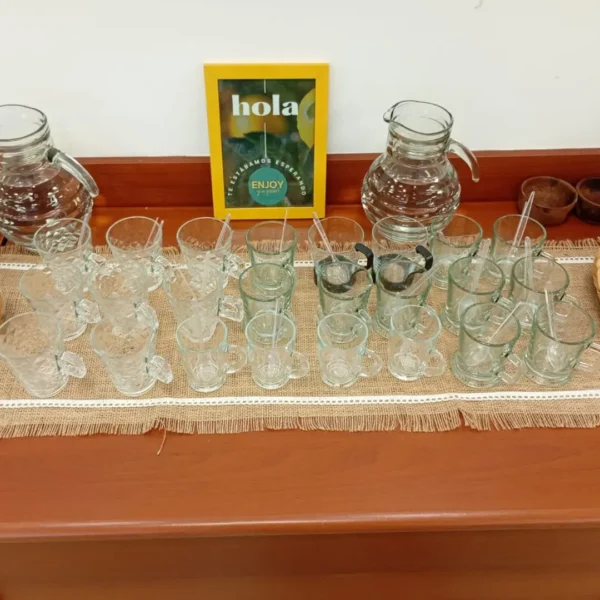 Estación de vajilla con tazas de vidrio para buffet corporativo junto a un cuadro amarillo con el logo de Enjoy y a picar.