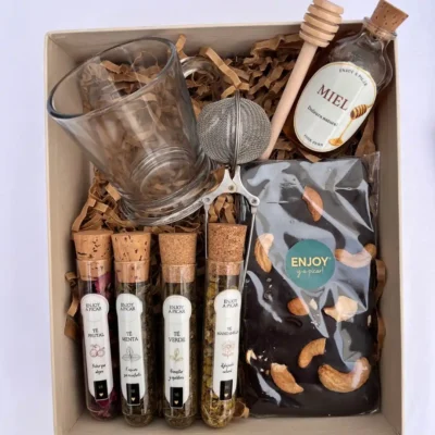 Box de regalo con taza de vidrio transparente, tubos de té en hebras, miel pura, chocolate artesanal y cuchara dorada.