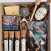 Vista cenital de box de merienda con blend de té en hebras, tomamiel de madera, cuchara dorada y brownie de chocolate.