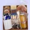 Box desayuno gourmet de regalo con taza blanca de cerámica, frascos de cookies y frutos secos, alfajores de maicena, brownie y café.