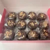 Vista superior de 12 alfajores artesanales bañados en chocolate semiamargo con lluvia de crocante en caja rígida.