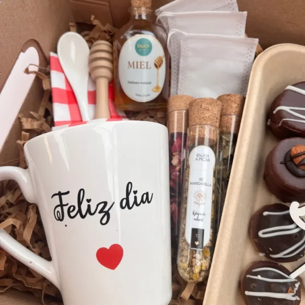 Detalle de taza de cerámica Feliz Día con corazón rojo, tubos de té manzanilla y rosas, miel pura y delicias dulces decoradas.