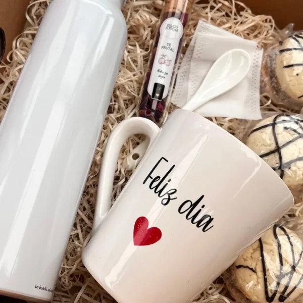 Primer plano de taza de cerámica Feliz Día con corazón rojo, cuchara y tubo de té frutal en hebras Enjoy a Picar.