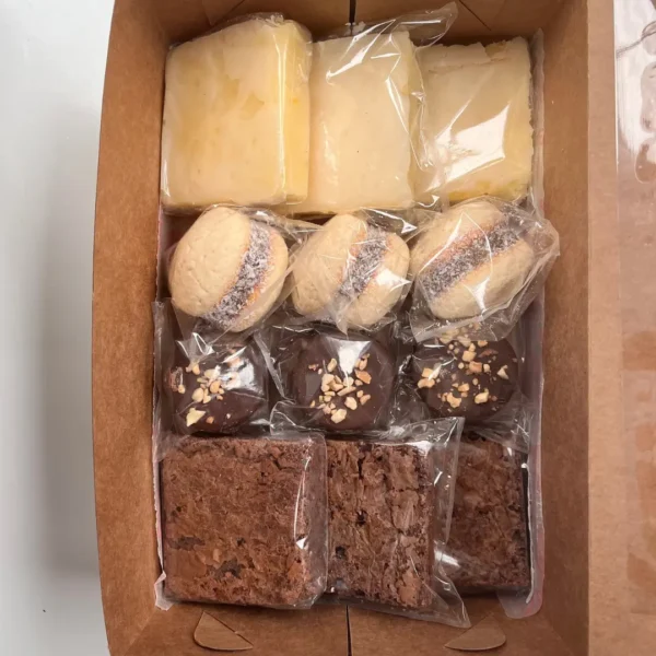 Primer plano de variedad dulce artesanal con alfajores rellenos con dulce de leche, bocados de limón glaseados y cuadrados de brownie con nuez.
